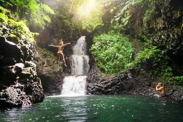 Couple jumping into water at Samoan waterfall swimming hole 