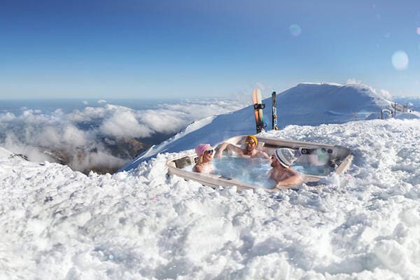 Three people in a mountain spa surrounded by snow