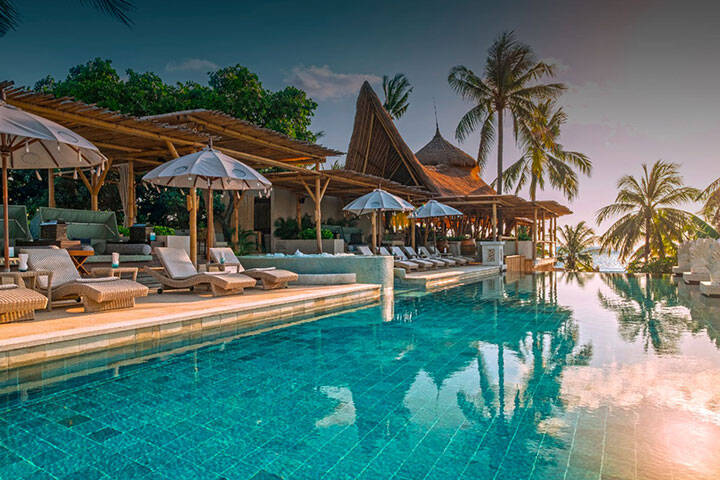 Beach chairs, umbrellas and palm trees surrounding the pool at Azul Beach Club, Bali