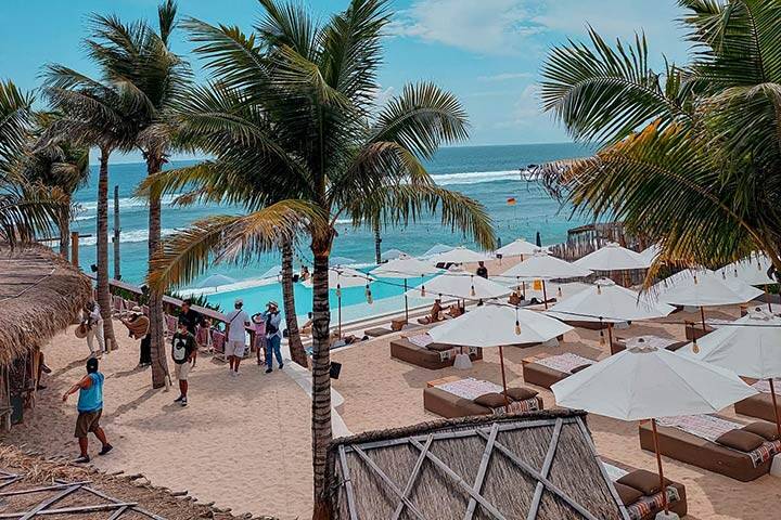 View of swimming pool and lounge areas on sand with palm trees at Palmilla Beach Club, Bali