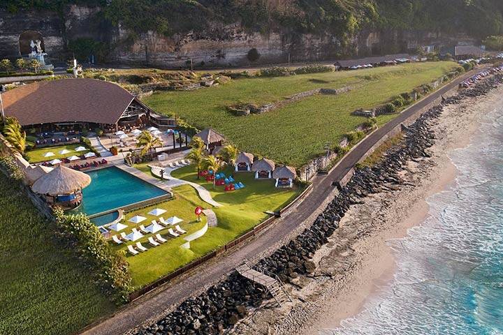 Aerial view of swimming pool and lush greenery overlooking ocean at Rooster Beach Club, Bali