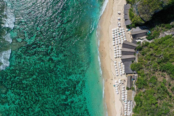 Aerial view of waves on sand and beach cabanas at Sundays Beach Club, Bali