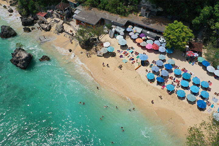 Aerial view of white sand beach, aqua water and colourful umbrellas at Padang Padang Beach, Bali