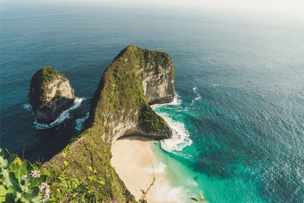 Aerial photo of green island and calm water at Kelingking beach in Nusa Penida, by Paolo Nicolello