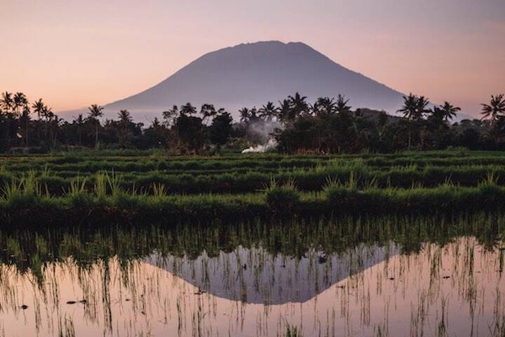 Sunrise behind mountain overlooking water puddles in Rendang Rice Fields Karangasem, Bali