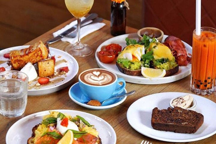 A table of breakfast food, including poached eggs and avocado on toast, coffee and fresh juice and Milk & Madu in Ubud, Bali