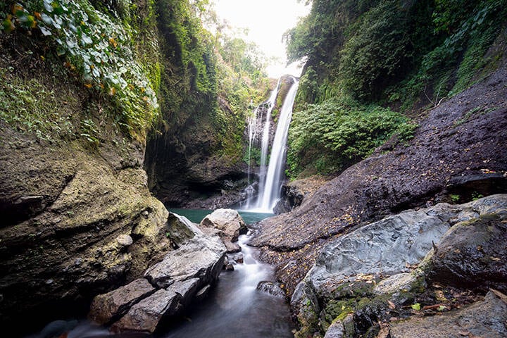 Water stream flowing down into rocks with rainforest surrounding at Aling-Aling Waterfall, Bali
