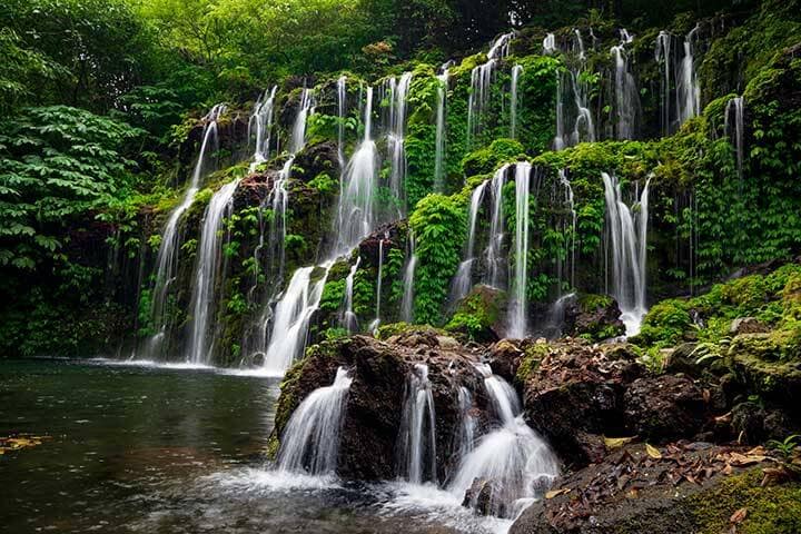 Multiple water streams flowing down onto lush greenery at Banyu Waba Amertha Waterfall, Bali