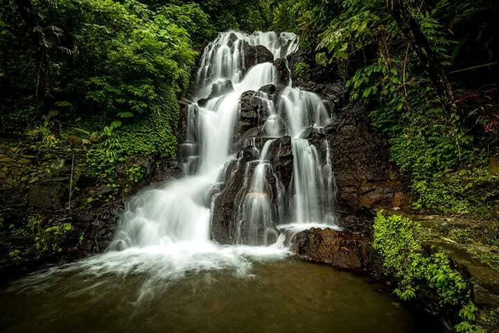 Water gushing down over rocks and trees at Jembong Waterfall, Bali