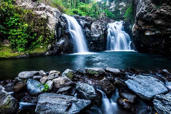 Two streams of water gushing down into blue watered swimming hole at Kembar Waterfall, Bali