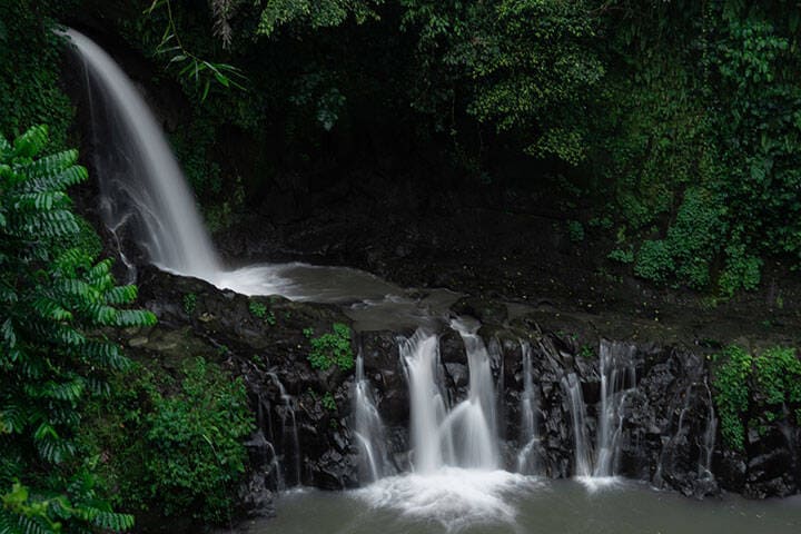 Multiple water streams flowing down into blue watered swimming hole at Taman Sari Waterfall, Bali