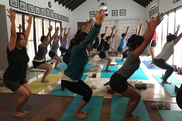 Students in lunge position with hands in air following instructor at Olop Iyengar Yoga Studio Seminyak, Bali