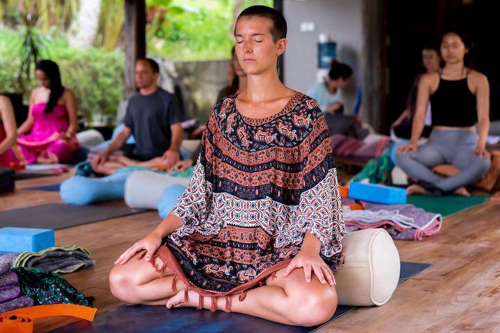 Women in yoga studio sitting on mats in seated position closing eyes and meditating at Zuna Yoga Ubud, Bali