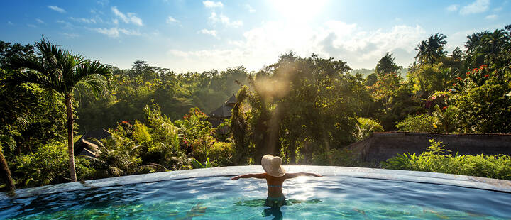 Woman swimming in an infinity pool overlooking forests on a clear, sunny day