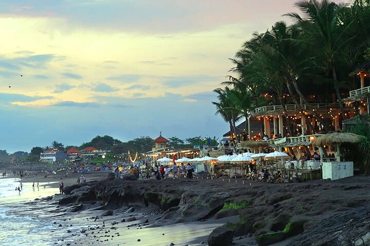 A beautiful beach club decorated with golden light bulbs. A restaurant on the rocks on ocean shore in tropical paradise. Illumination of cafe after sunset. Happy vacation background. Bali lifestyle.