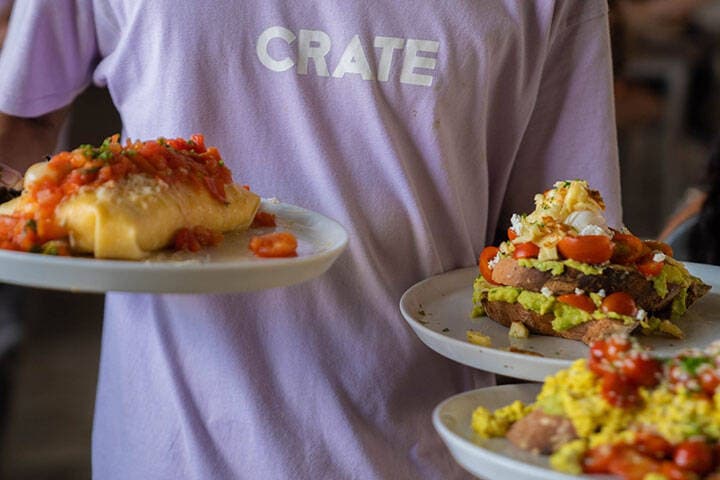 Waiter carrying three plates serving breakfast omelettes at Crate Cafe Canggu, Bali