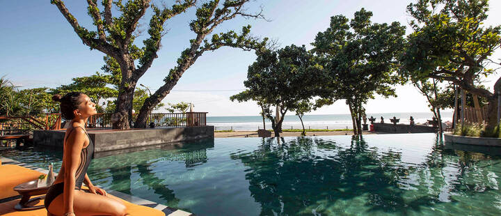 Woman relaxing in hotel swimming pool overlooking beach at hotel in Seminyak