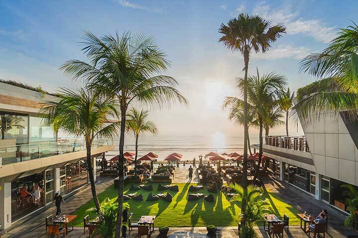 Sun lounges with umbrellas overlooking pool and beach at Ku De Ta Seminyak, Bali