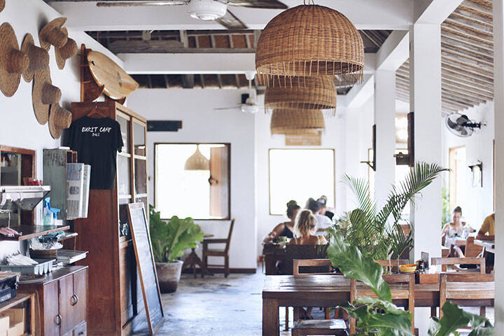 Indoor dining area with hanging rattan lights over tables and chairs at Bukit Cafe Uluwatu, Bali