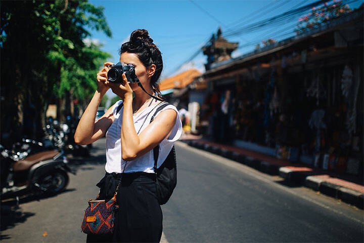 A young woman, a solo tourist, walking the streets and taking pictures on her camera in Ubud on the island of Bali, Indonesia