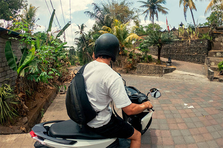 A young Caucasian man sitting on a motor scooter, stopped at a crossroad junction while exploring Bali