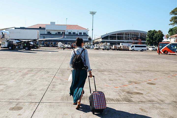 Young woman arriving at Bali Island international airport in Denpasar, wearing casual clothing with a suitcase and backpack