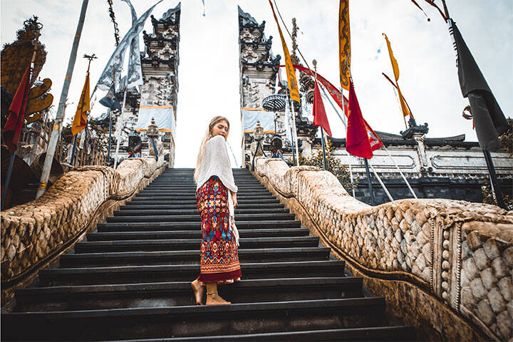 A woman in a long skirt and shawl standing at the ancient gates of Pura Lempuyang Bali