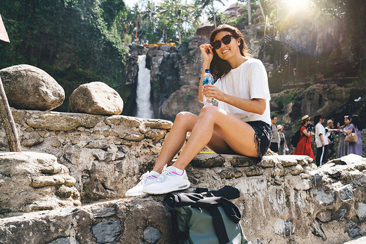 Young woman wearing a T-shirt, denim shorts and exercise sneakers at a waterfall in Bali