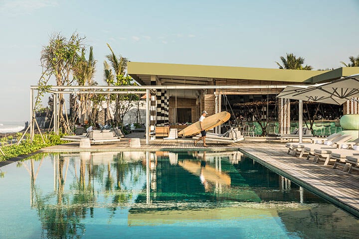 Man walking with surfboard by the pool at COMO Uma, Canggu Bali