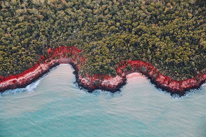 Aerial view of Rainbow Beach at Tiwi Islands. A quick boat ride from Darwin lies the peculiarly pink shores of Melville Island, Tiwi Islands. Populated by the hilariously cheeky Indigenous Tiwis, stepping onto the Islands is like stepping back in time. Sweeping rusty dirt roads meander through the eucalypt forest and are interspersed only by small communities and freshwater springs.
