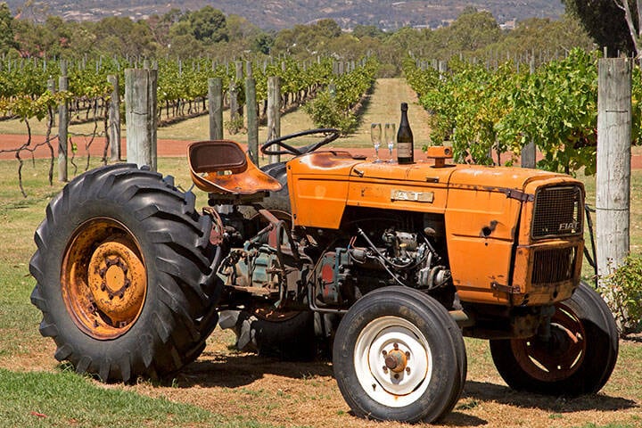 A tractor with wine glasses and a bottle placed on top sits in front of the vineyards at Ugly Duckling Wines in Swan Valley, Perth.