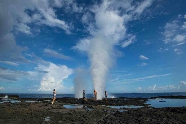 Travellers playing on rocks with blow hole water, Samoa