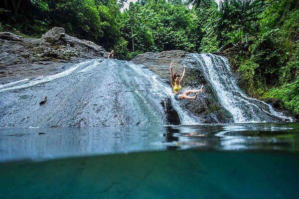 Travellers sliding off rock into water, Samoa