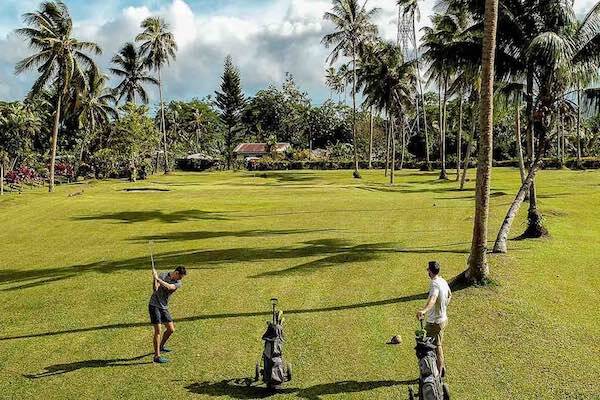 Travellers playing golf on green course surrounded by palm trees, Samoa