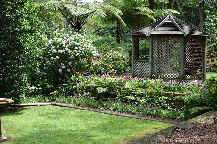 A charming gazebo nestled among the trees in Lisgar Gardens, surrounded by lush foliage and vibrant flowers. The tranquil setting invites visitors to relax and enjoy the natural beauty of the garden, creating a peaceful escape.