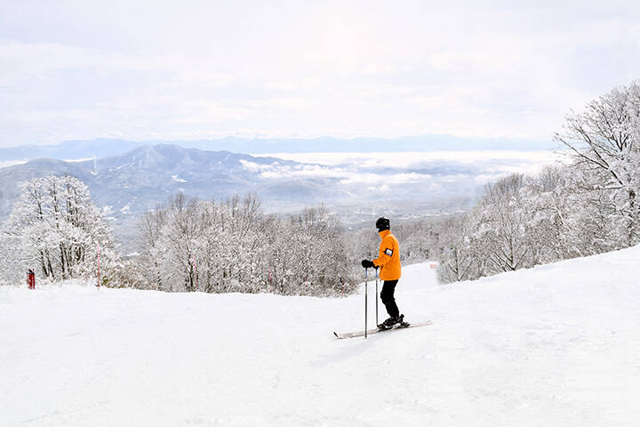 Skier taking in the beautiful Myoko scenery before continuing down the mountain. Distant mountain ranges are partially covered by low lying clouds.