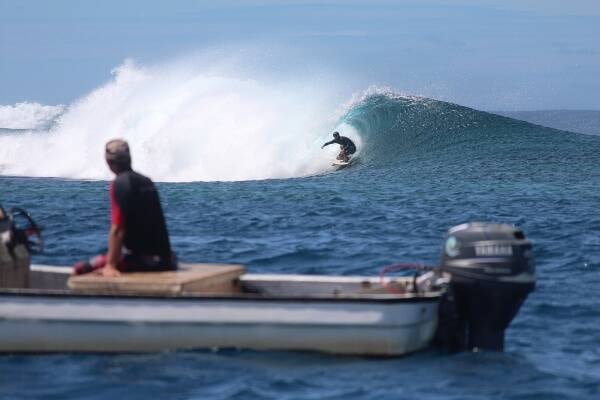 Man in boat watching surfer ride wave in blue ocean, Samoa