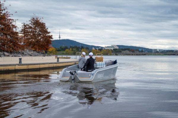 View of people in electric boat floating on lake with silhouette of Black Mountain tower in background