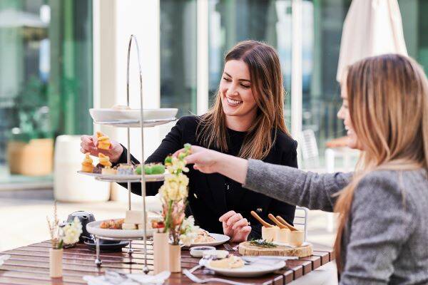 Two young women with tea stand of high tea foods at Parliament House
