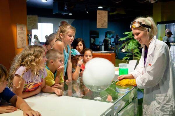 Female scientist in white coat showing children a science experiment at Questacon in Canberra