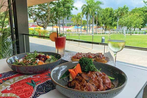 Dishes placed on table overlooking green grass and palm trees at Curve Cafe and Bar in Darwin.
