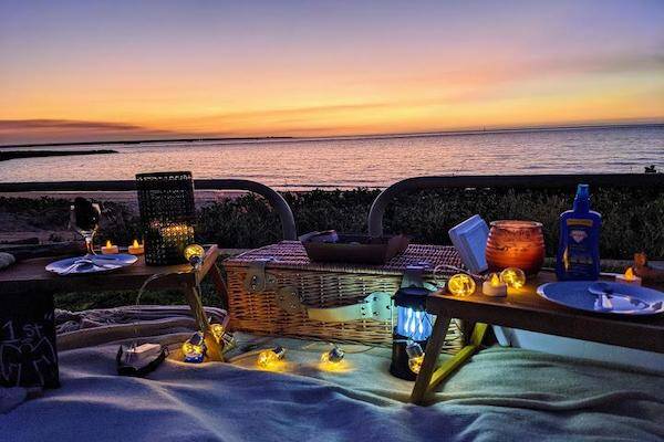 Picnic setup with tables, drinks, lighting and basket overlooking beach sunset at Cullen, Darwin.