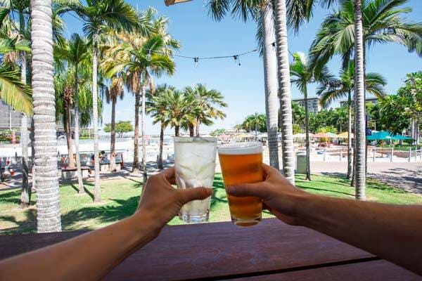 Friends clinking glasses to cheers, overlooking palm trees and greenery at The Precinct, Darwin.
