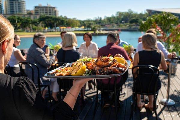 Server bringing out platter of seafood to guests enjoying their lunch overlooking the water at Wharf One & Bella Darwin.