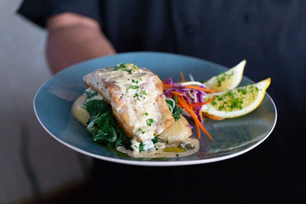 Waitress carrying plate of freshly cooked fish on salad with lemon, at Yots Greek Taverna, Darwin.