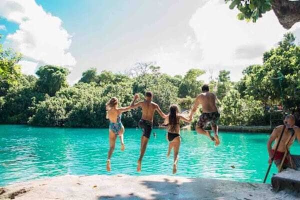 Travellers jumping off rock into blue lagoon, Vanuatu