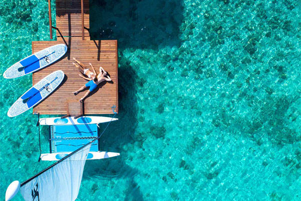 Couple sunbathing on a boardwalk at The Havannah, Vanuatu, surrounded by turquoise water