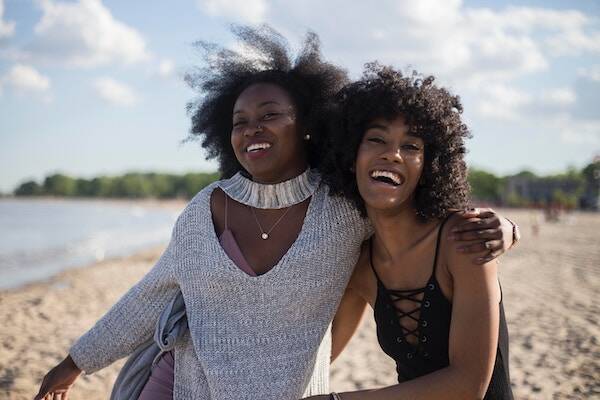 Friends holding each other and walking along sand on beach, Vanuatu 