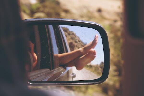 Reflection in car side mirror of feet hanging out of car on road trip, Vanuatu 