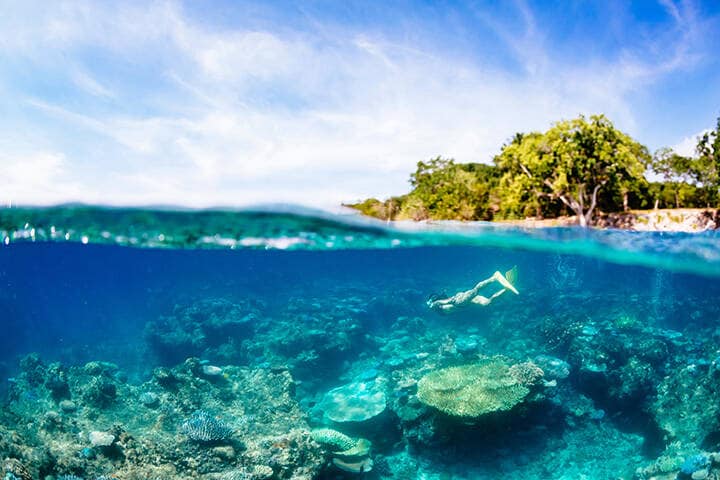 A woman snorkelling over a coral  reef off the coast of Espiritu Santo, Vanuatu.